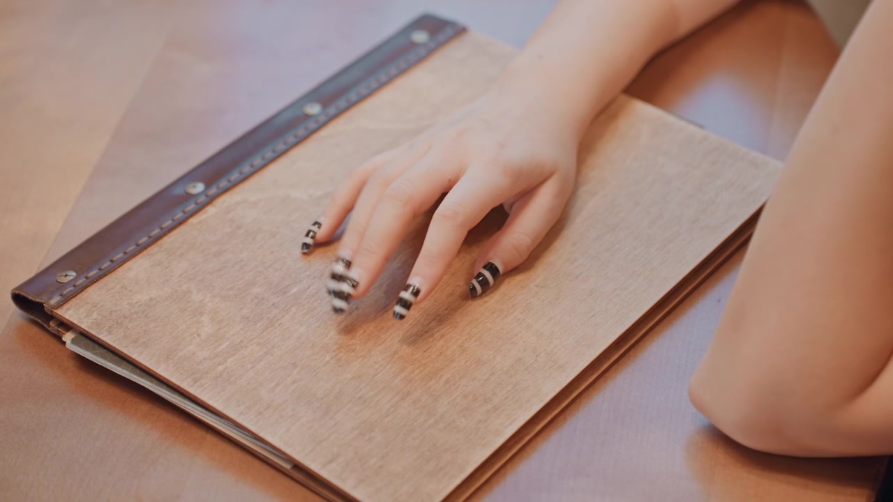 Mano con unghie a strisce su un quaderno, nail artist testa lo smalto, scrittrice si ferma mentre scrive sul diario, stilista inquadra una posa sotto una calda luce da studio, dettaglio ravvicinato della manicure e della copertina testurizzata.