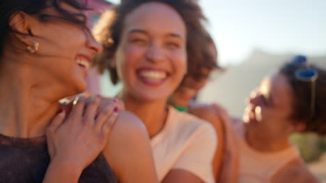 Portrait-Of-Laughing-Female-Friends-Standing-And-Hugging-By-Open-Top-Car-On-Road-Trip