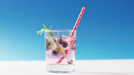 Close-up-of-transparent-drink-with-bluberries-on-blue-background