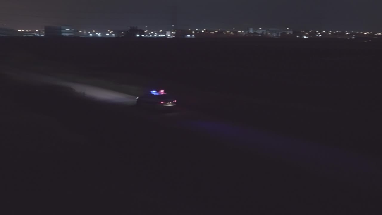 Night aerial footage of a police car driving down a dark urban area