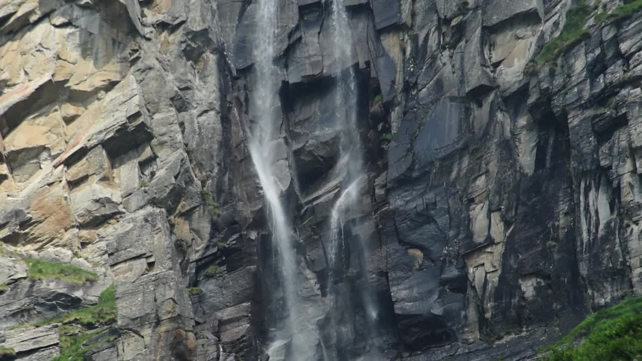 cerca de una cascada alpina que desciende por un acantilado rocoso, con un árbol solitario de pie alto contra un telón de fondo de montaña alpina