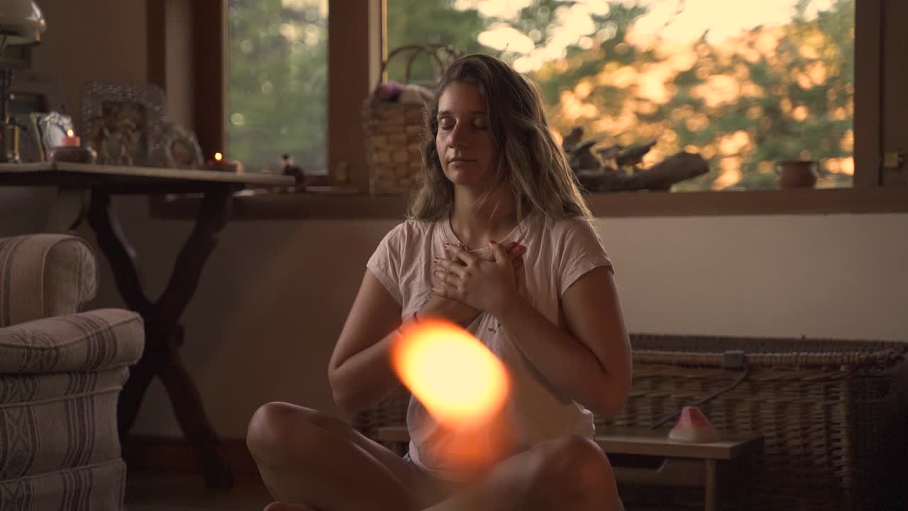 Young female latin meditating sitting on a pillow in casual indoor spiritual studio with candles, window with vegetation in a wooden home2 slow motion 60fps