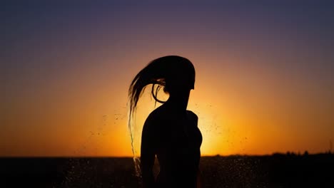 a mesmerizing silhouette of a woman dancing joyfully amidst a cascade of droplets, illuminated by the warm glow of a stunning sunset on the horizon
