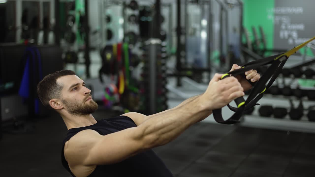 vista lateral de un deportista fuerte haciendo ejercicios con correas de trx en el gimnasio