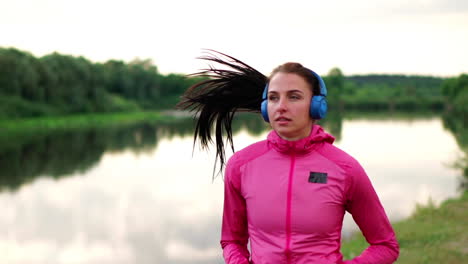 a girl in a pink jacket and black pants runs near the river in headphones preparing for the marathon