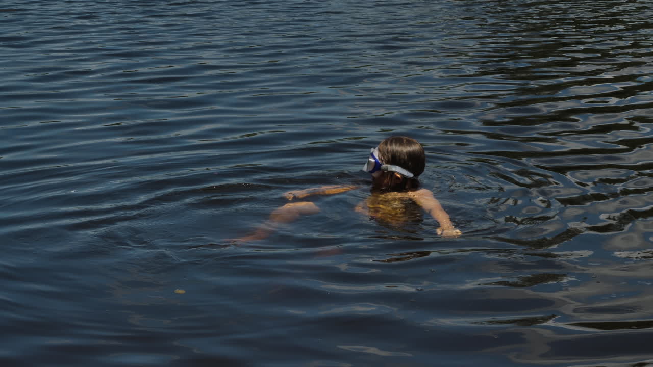 niño con gafas de protección en la cabeza bañándose en un lago
