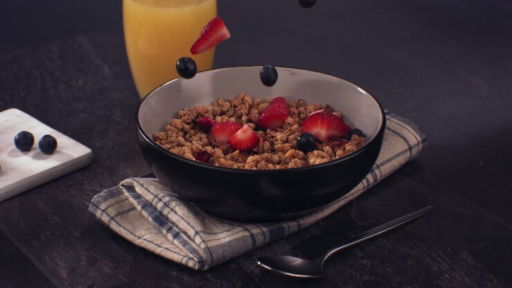 SUPERZEITLUPE: Frische Erdbeerscheiben und Blaubeeren fallen in eine Granola-Müslischale. Aufgenommen mit Hochgeschwindigkeitskamera bei 420 FPS