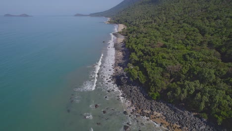 olas del océano salpicando en la costa rocosa de la playa fronteriza en wangetti, qld, australia - retroceso aéreo