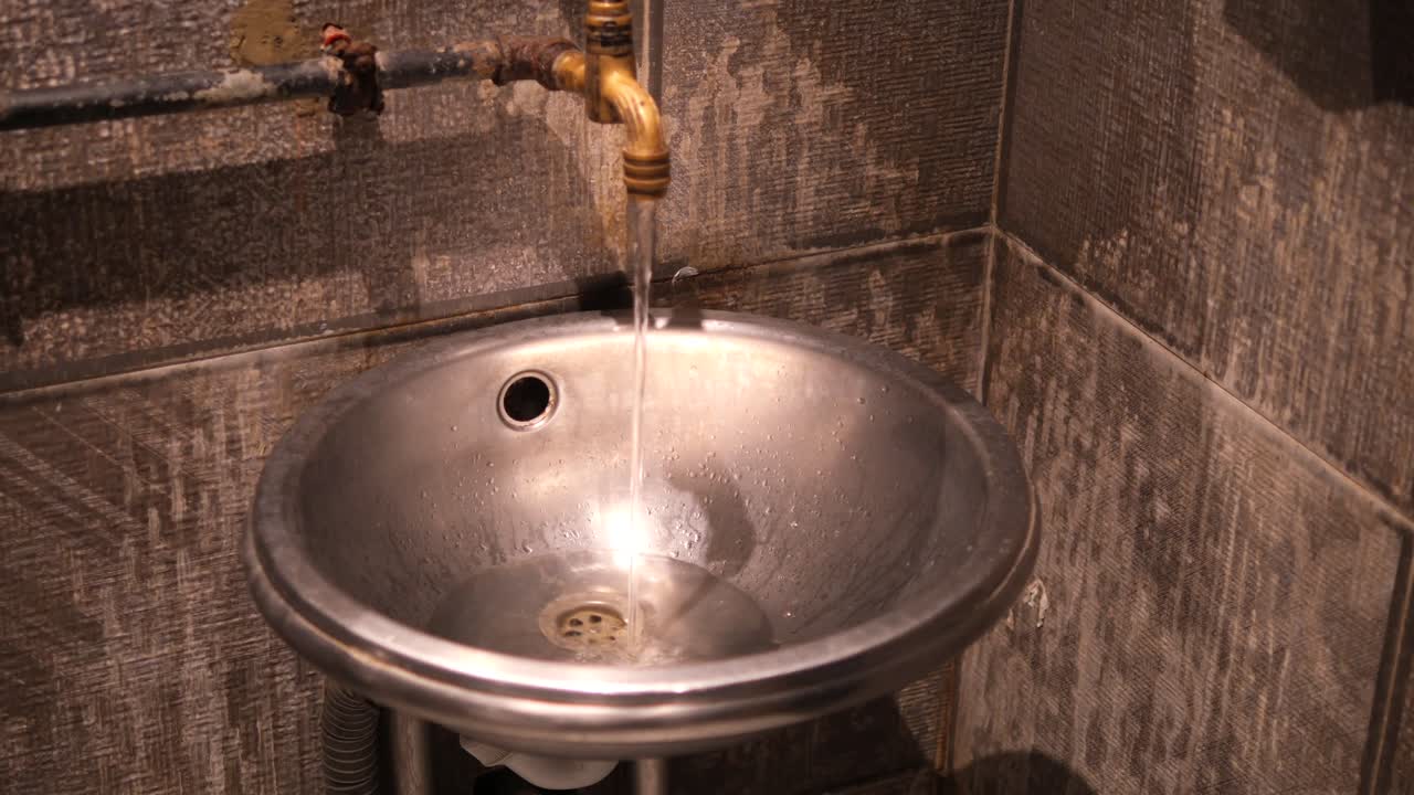 A stainless steel sink with a brass faucet, water running into it in a bathroom setting