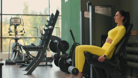 fuerte deportiva hispana morena haciendo ejercicio de piernas en un simulador deportivo en un club de fitness. con ropa deportiva amarilla. mujer atlética realiza un ejercicio de extensión de piernas en el simulador