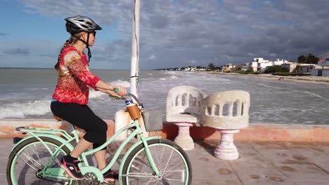 closeup de mulher madura andando de bicicleta cruiser em um píer com um mar ao fundo