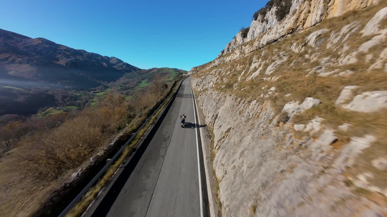 FPV drone performs a wide orbit and trailing shot of a motorbike in motion, surrounded by green hills and soft valley mist.