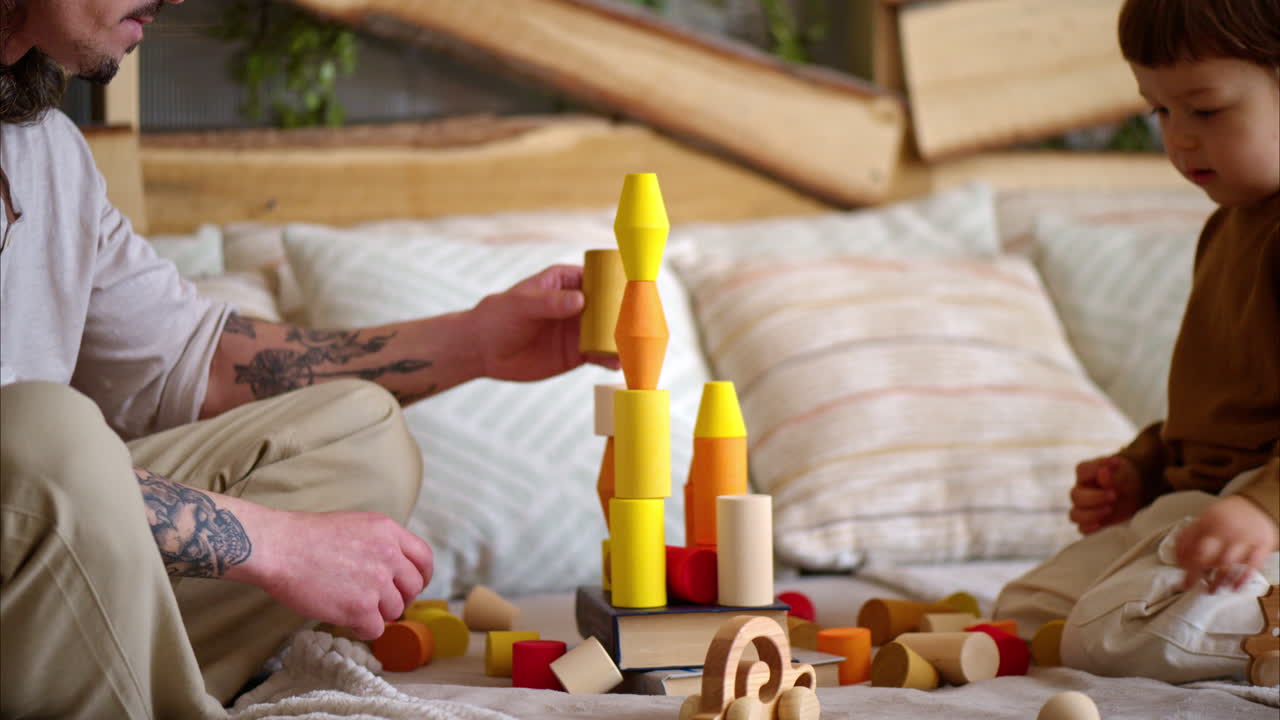 Father playing with his son with colourful, ecological wooden toys on the bed