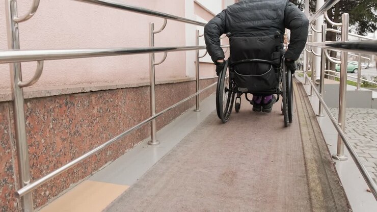 Una persona con disabilità si muove lungo la strada in sedia a rotelle, sale sulla rampa.