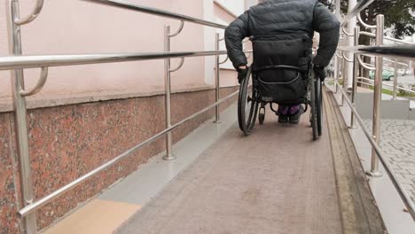 a person with a disability moves along the street in a wheelchair, climbs the ramp