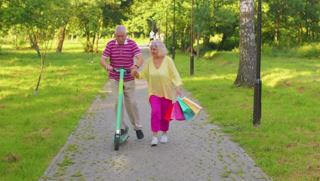 senior stylish couple grandmother, grandfather after shopping with bags using scooter for riding