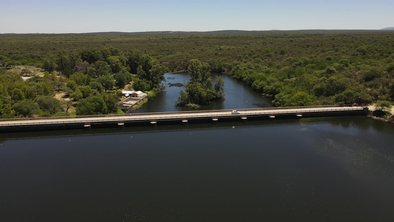 vista aérea que muestra el cruce del lago por el puente de la represa en córdoba, argentina - hermoso paisaje forestal en el fondo durante el verano