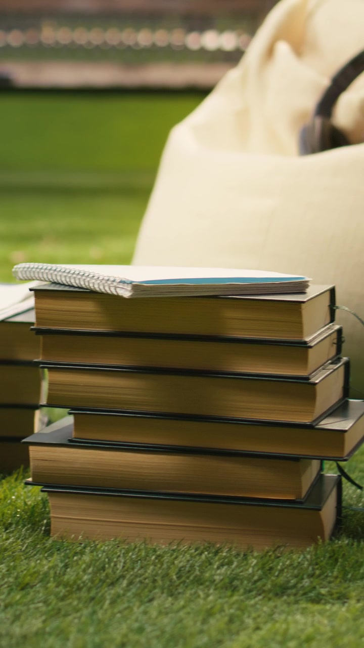 Vertical Video Stacked books and headphones placed on soft beanbag in sunny outdoor campus