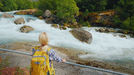 una mujer joven parada junto a la cerca mira el agua de deshielo del río de montaña escarpada que corre desde el briksda