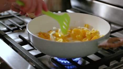 woman stirring frying pan filled with onions and peppers in slow motion