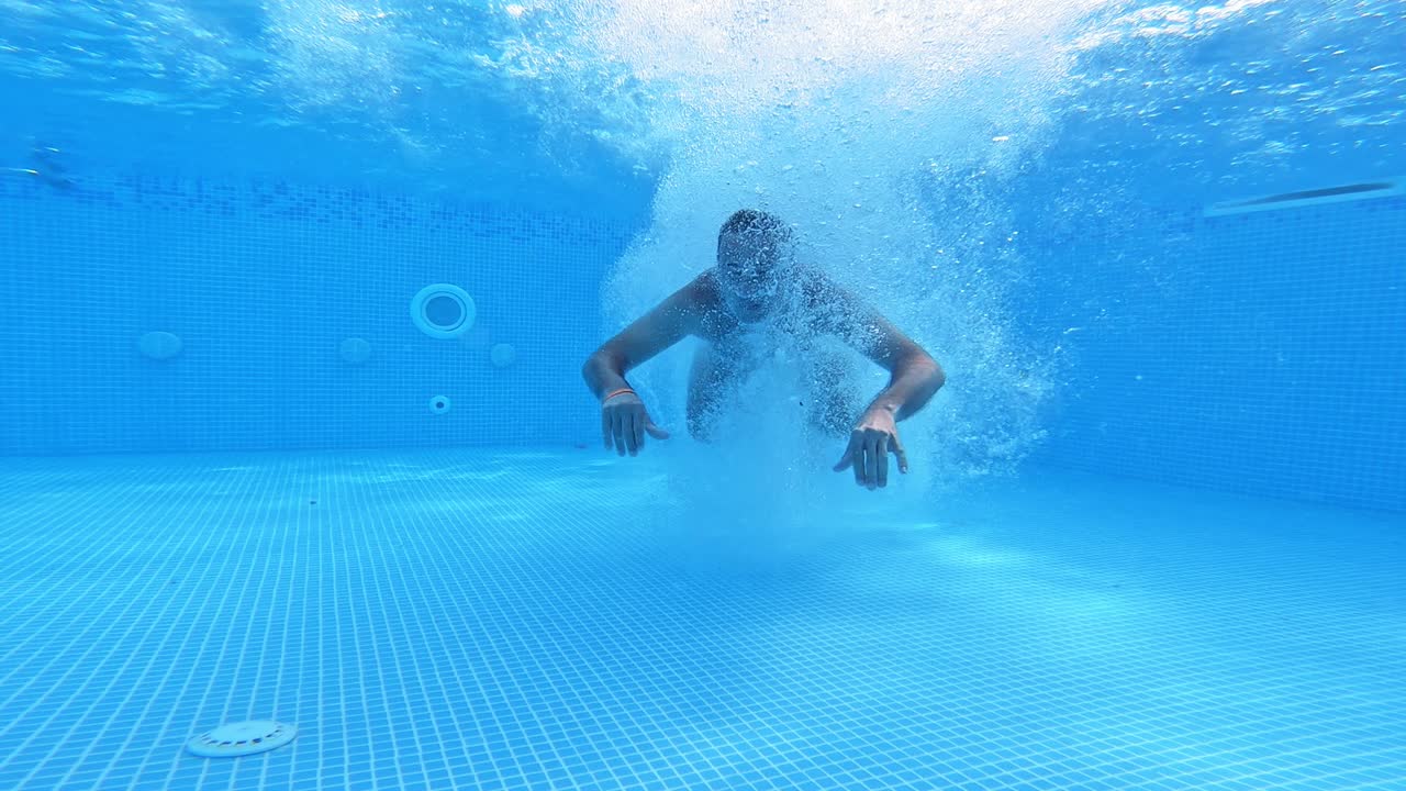 Man jumps under water in the pool. Underwater view on a man diving into water and swimming inside the swimming pool.