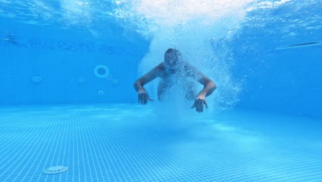 man jumps under water in the pool. underwater view on a man diving into water and swimming inside the swimming pool.