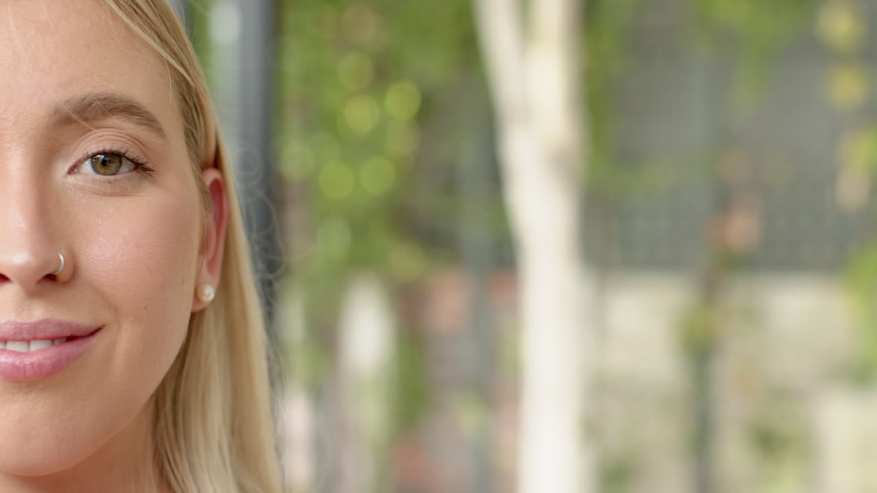 Smiling young woman with nose ring and earrings, enjoying outdoor setting, copy space