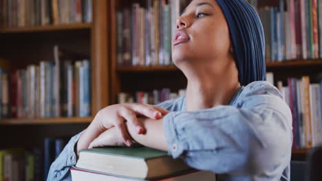 Asian-female-student-wearing-a-blue-hijab-sitting-and-leaning-on-a-pile-of-books-and-thinking