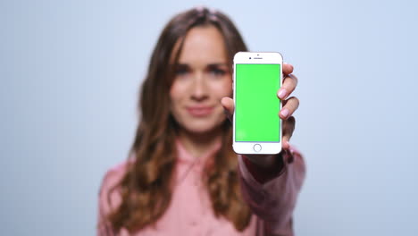 Businesswoman-showing-smartphone-with-green-screen-in-studio