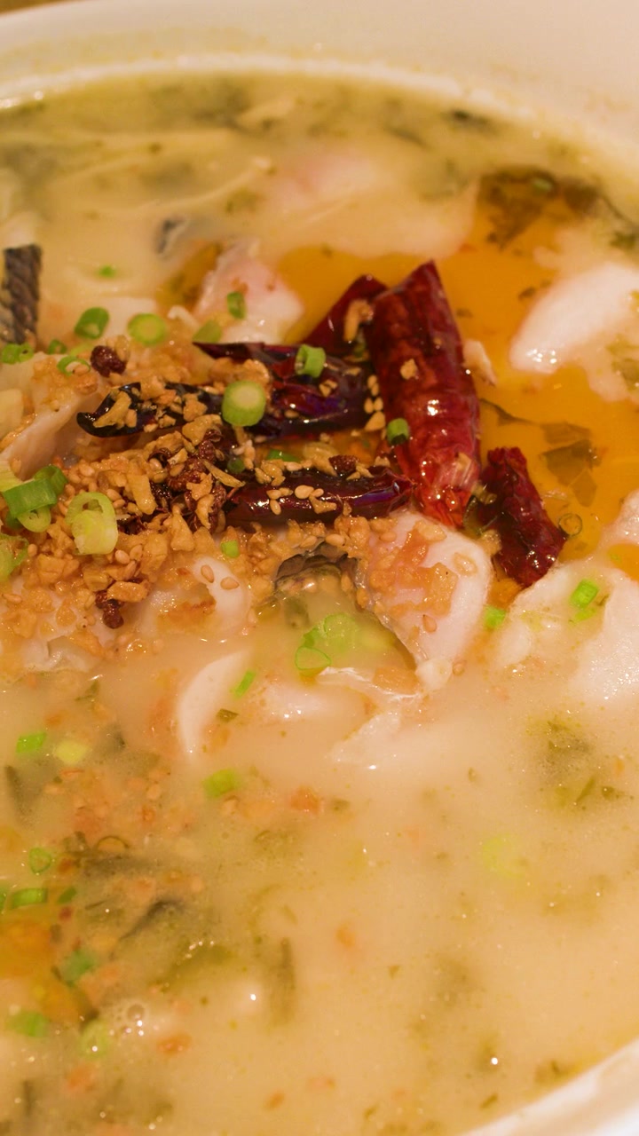 Primo piano di zuppa di pesce del Sichuan fumante con peperoncini secchi ed erbe aromatiche in una ciotola bianca.
