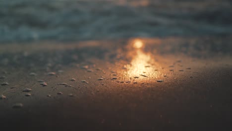 slow motion of the sea water flooding the reflection of the sunset on the shoreline during golden hour. close-up with blurry background