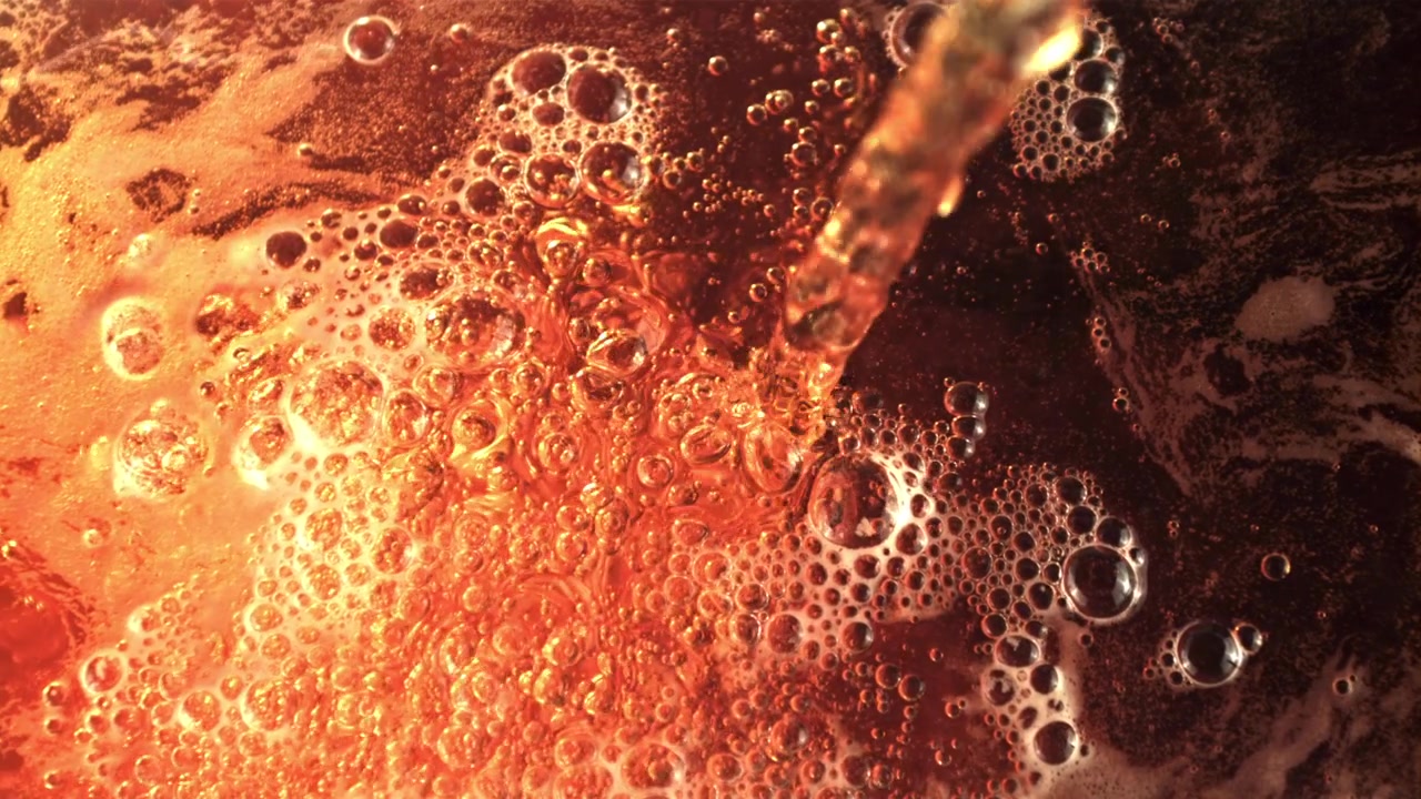Primo piano di liquido dorato versato che crea numerose bolle