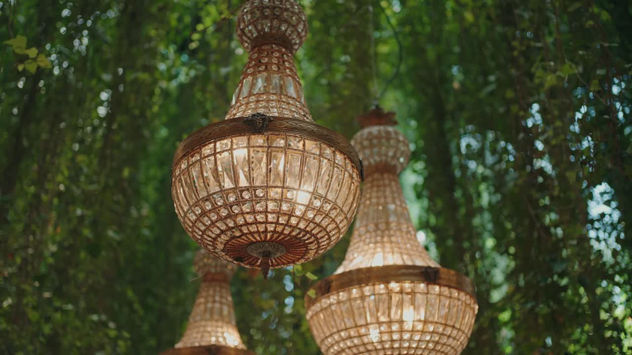 ornate crystal chandeliers illuminate with warm light against greenery backdrop