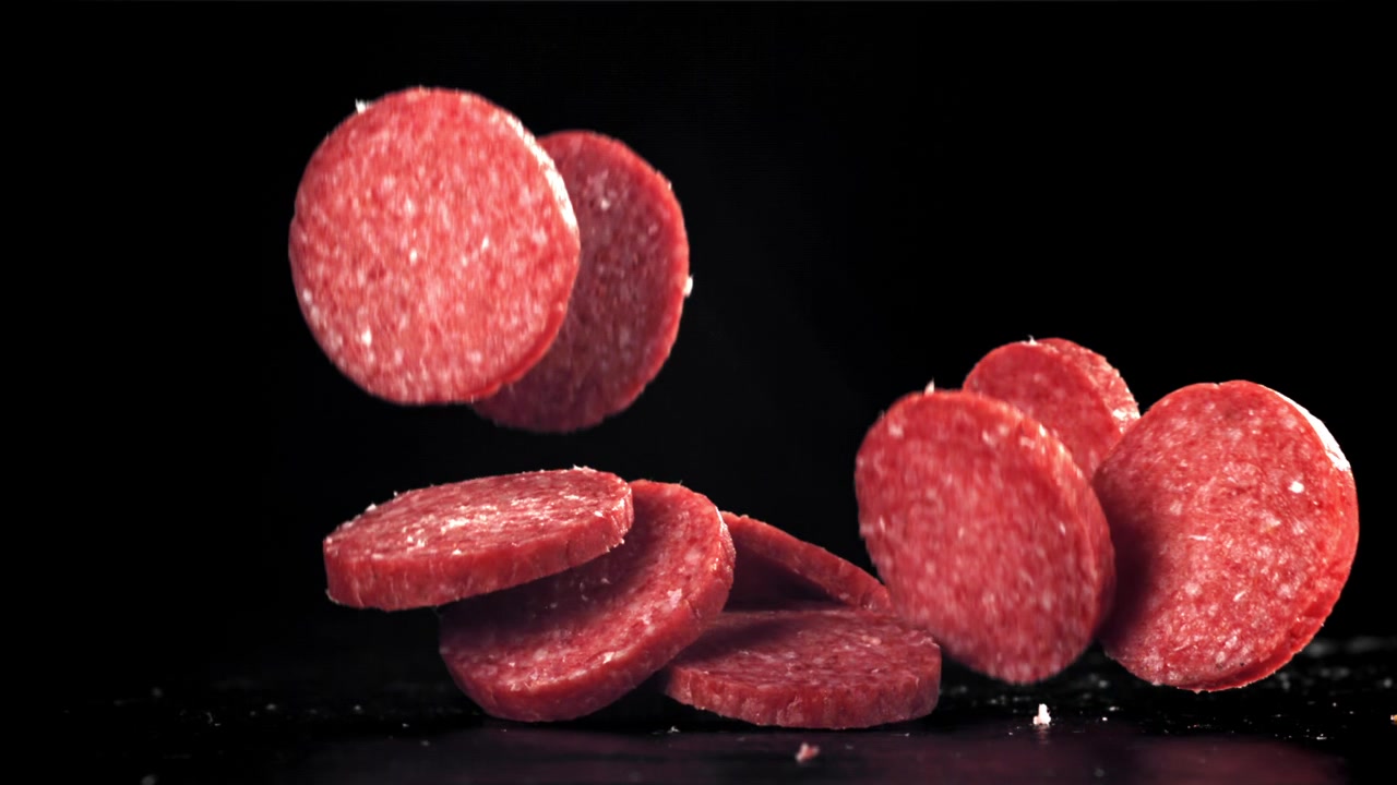 Fette di salame rosso che cadono al rallentatore su sfondo nero