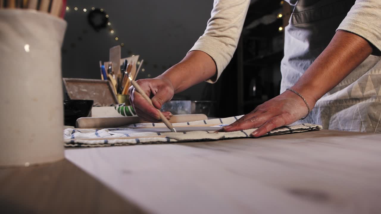 Pottery in the studio - young woman cuts off the excess of the clay using a tool