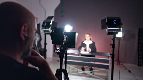 backstage of the photo studio work. male cameraman sits at camera recoding video of a female reporter.