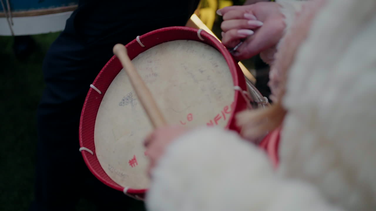 persona tocando un tambor rojo con palos de madera durante un evento de música al aire libre