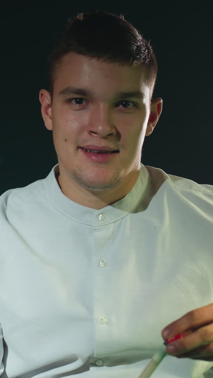 joven con camisa blanca contra un fondo oscuro sostiene cuidadosamente el palo de la pilla, aplicando la cubierta roja con expresión enfocada. la iluminación destaca la preparación, la concentración y la precisión en el billar