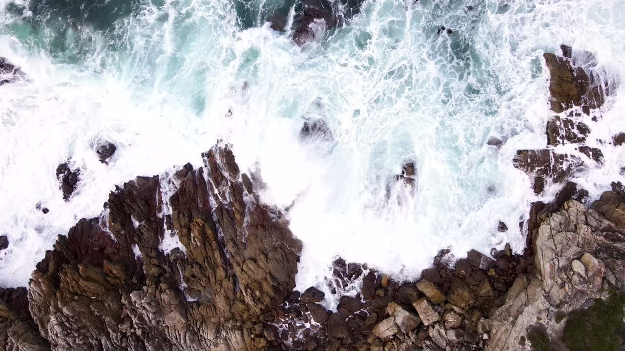 Atlantic ocean waves surge onto jagged coastline in slow motion, top down aerial