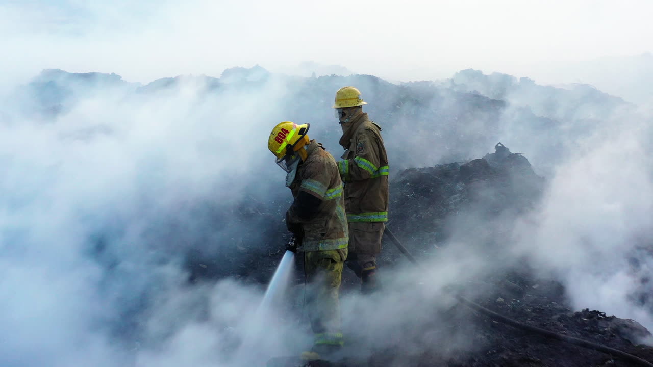 Aerial view of the fire department quelling a fire, fighters extinguishing in middle of rising smoke - Pull back drone shot