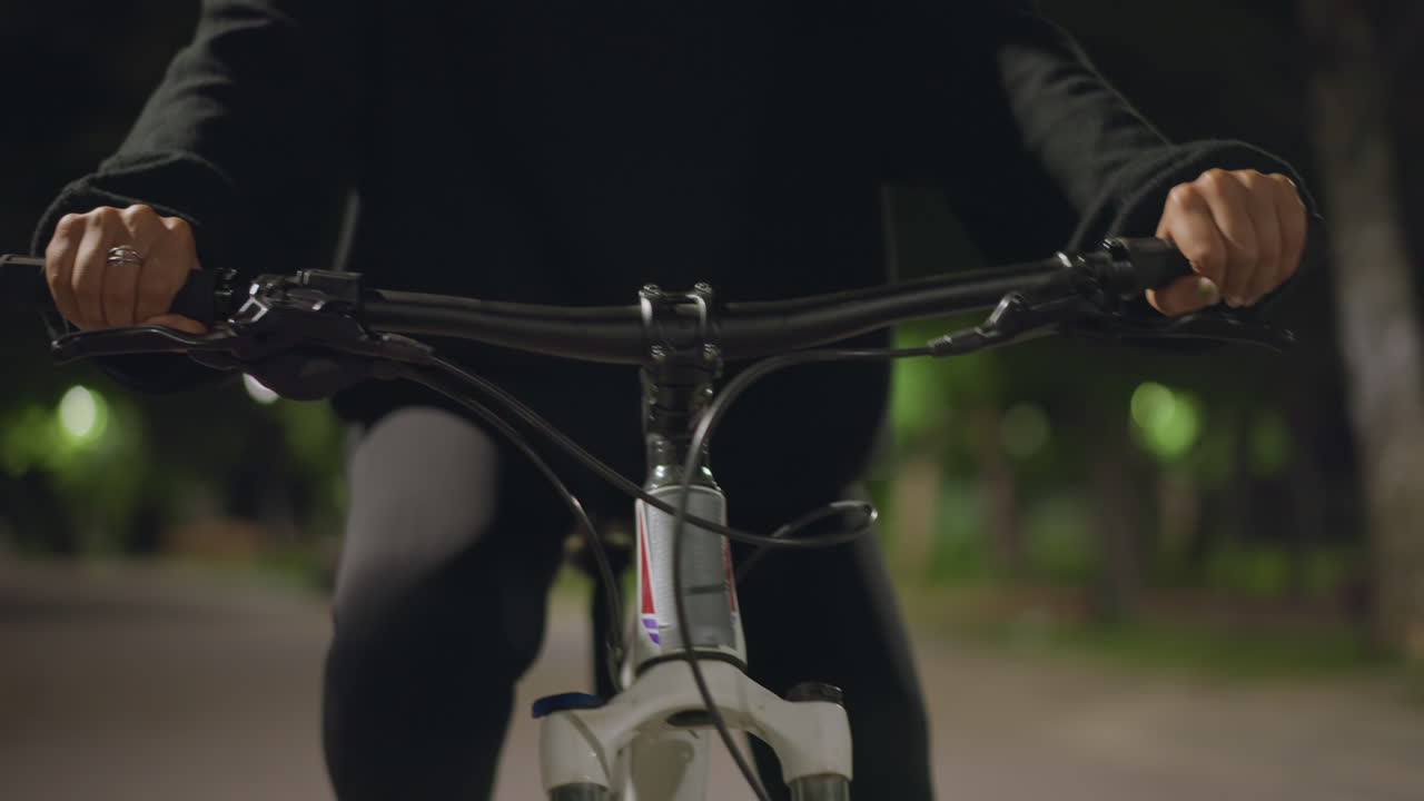 Steady Handlebar Control At Night, Calmly Steering Bicycle Along Lit Trail Under Nighttime Sky, Pushing Forward Intentionally With Firm Grip Along Softly Illuminated Park Pathway At Night