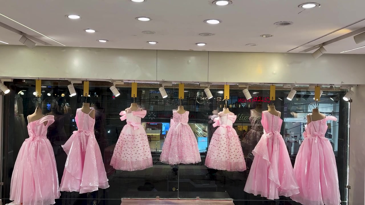 エレガントなピンクのフォーマルドレスが飾られた、高級子供服店のショーウィンドウ。