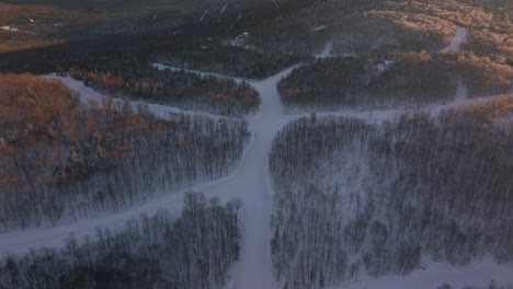 campos cubiertos de nieve con árboles densos en el sur de quebec canadá durante la puesta de sol - retroceso aéreo