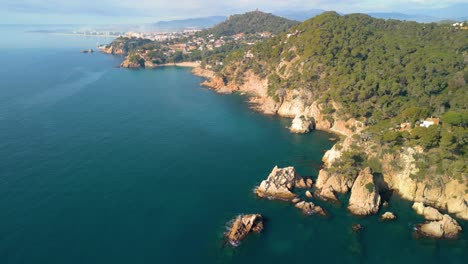 Discover-the-enchanting-beauty-of-Lloret-De-Mar's-beaches-from-the-sky,-capturing-the-clear-blue-sea-and-upscale-tourism-destinations-of-Santa-Cristina-and-Cala-Treumal