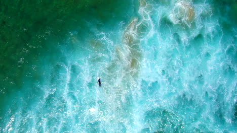 AERIAL-:-Birdseye-view-from-80-metres-of-surfer-battling-the-waves,-current-and-white-wash-in-a-turbulent-ocean