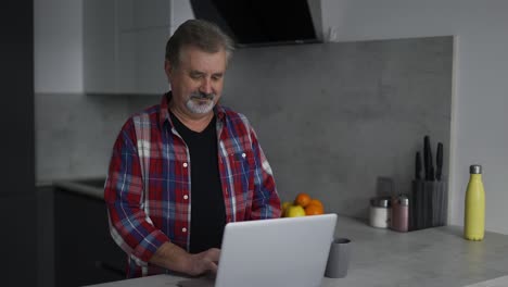 anciano barbudo usando una computadora portátil en la cocina