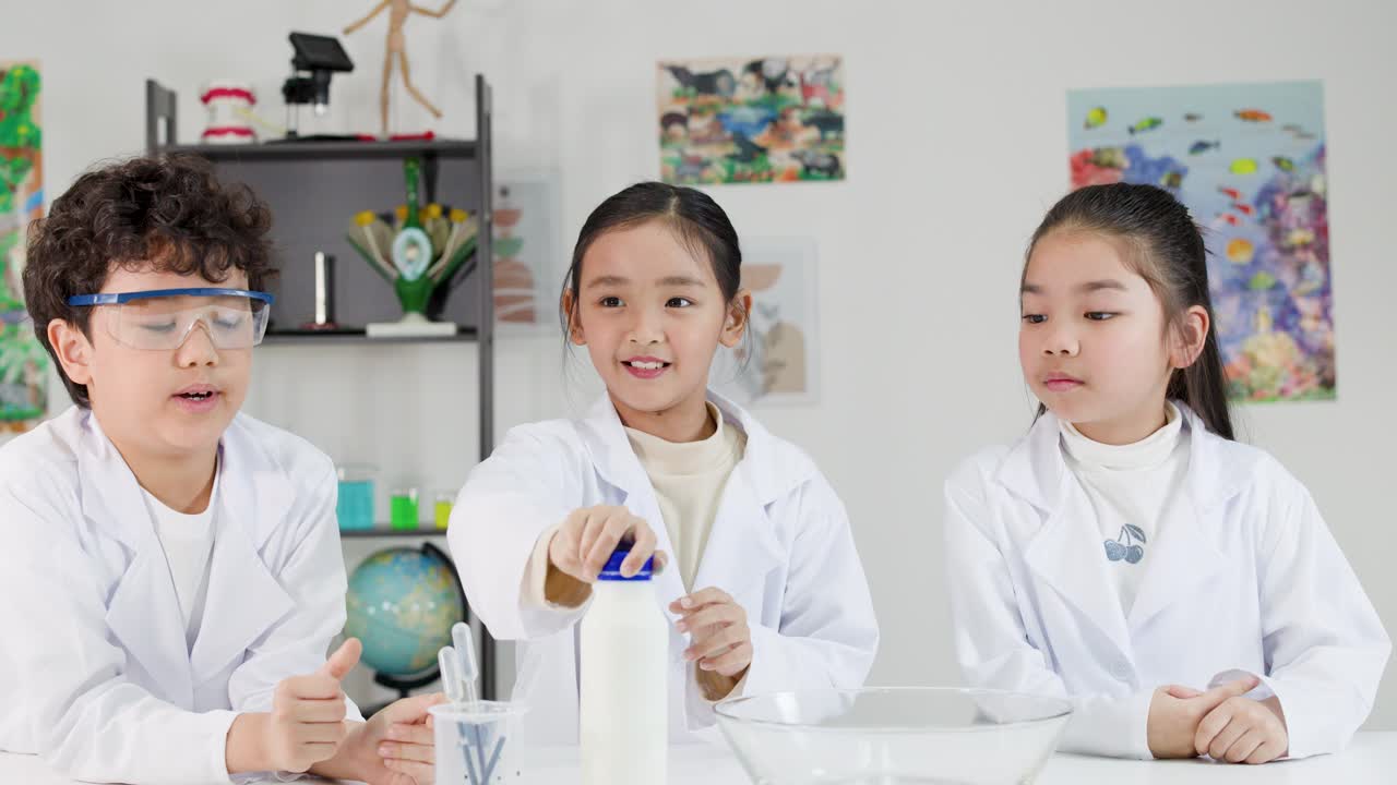 白衣と安全ゴーグルを着用した3人のタイの子供たちが、一緒に化学実験を行っています。
