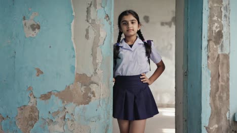 confident young student posing in decaying school building wearing uniform and backpack, symbolizing challenges faced by children in underprivileged educational environments