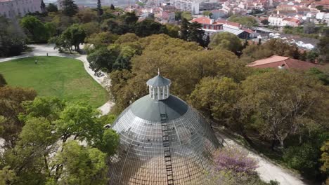 aerial circular orbit flying over beautiful crystal greenhouse in historical park in downtown lisbon, portugal