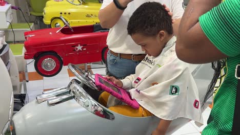 exótico y lindo niño negro, de tres años, cortándose el cabello en un salón de peluquería infantil mientras su madre lo consuela